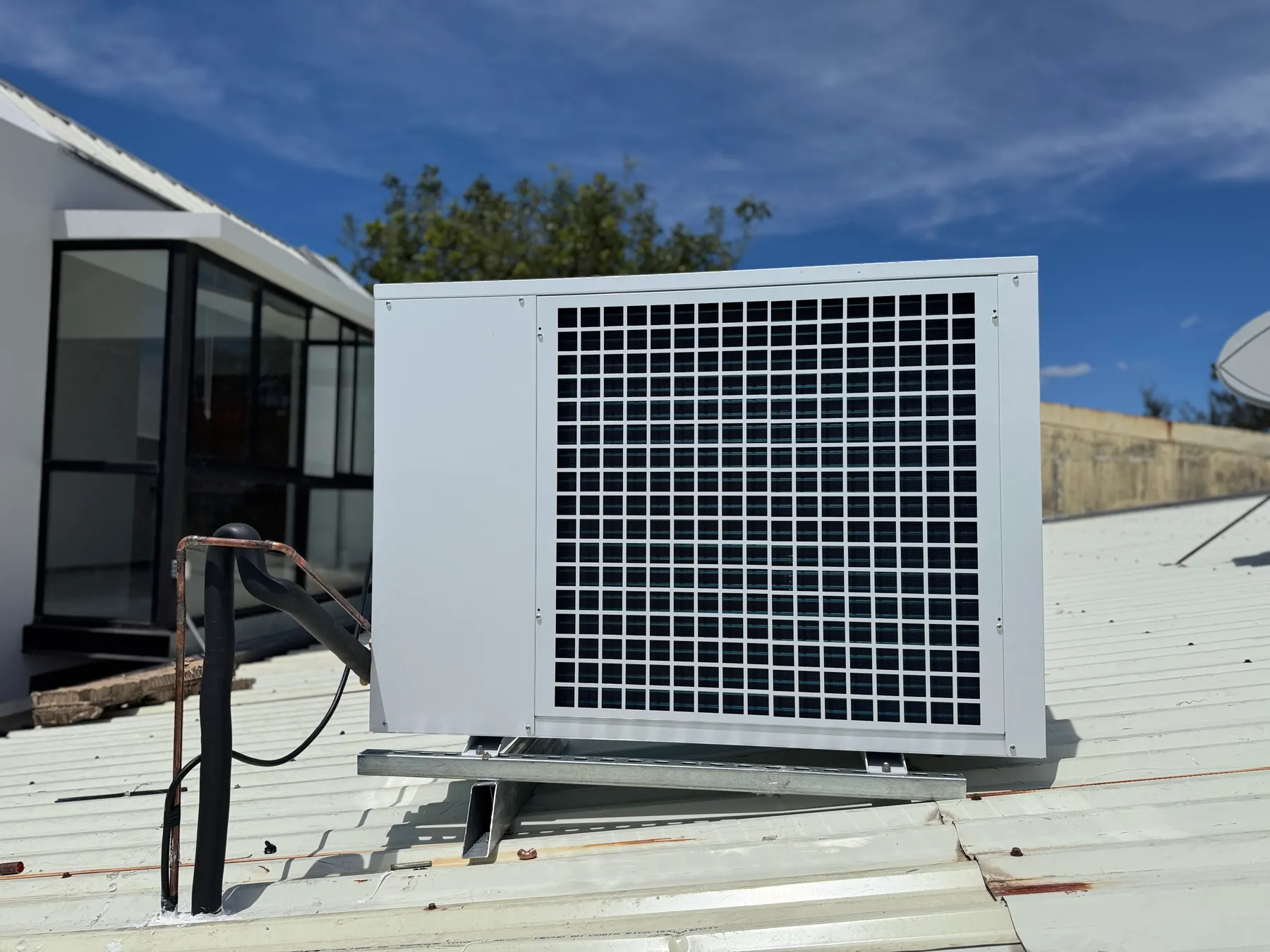 Outdoor air conditioning condenser installed on a metal roof under a clear blue sky