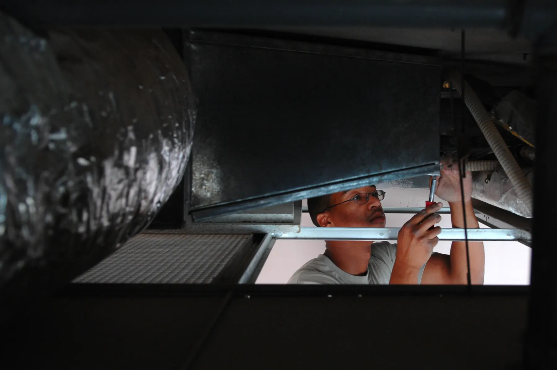 Technician checking a sheet metal duct connection above a ceiling