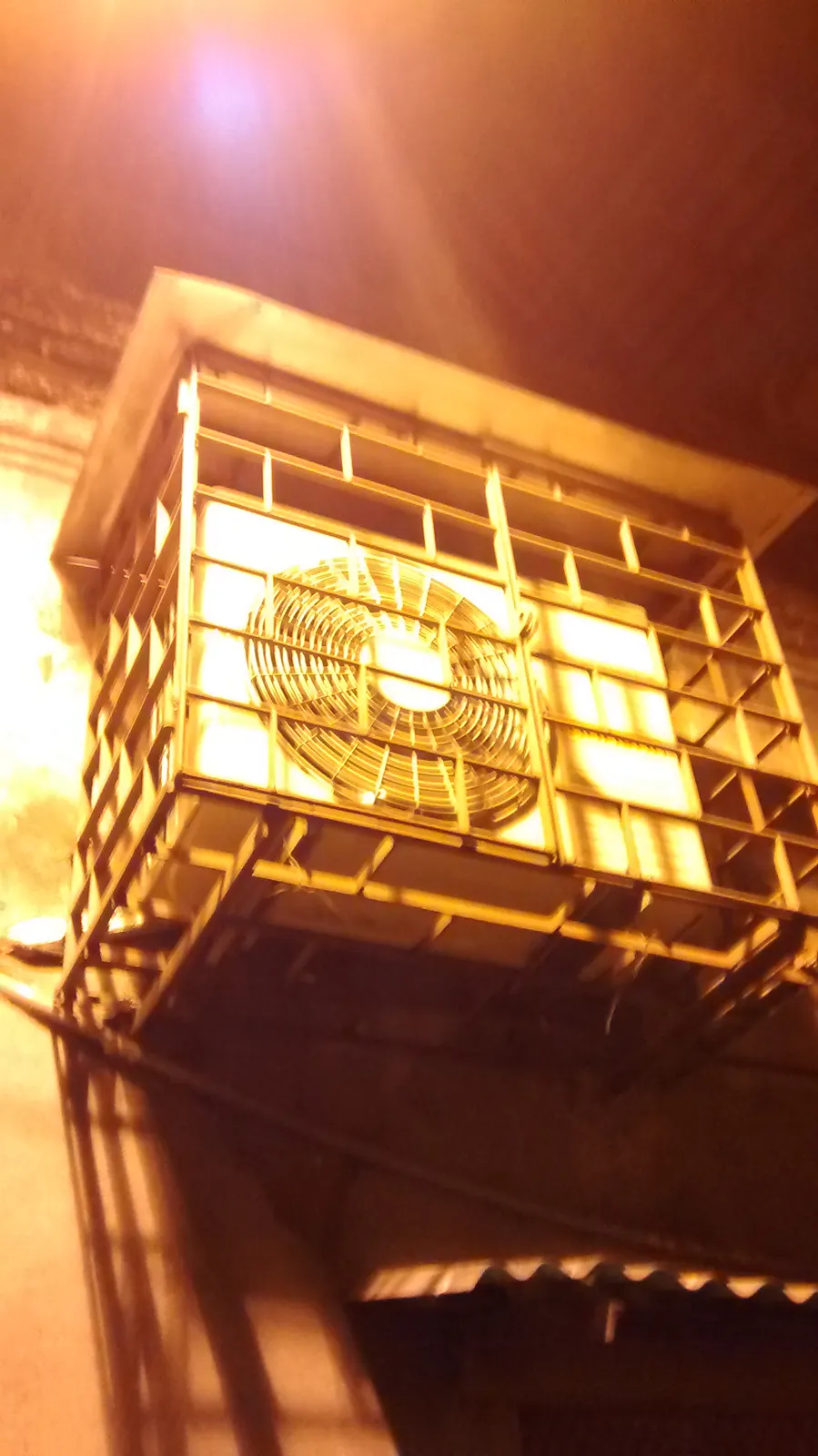Outdoor heat pump unit at dusk lit by a warm work light